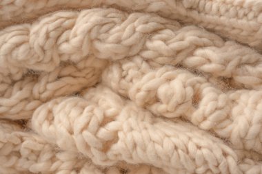 A fragment of beige knitted fabric, knitted from white sheep wool. Knitted background. 