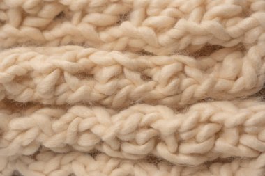 A fragment of beige knitted fabric, knitted from white sheep wool. Knitted background. 
