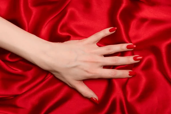 美しい赤マニキュア上の女性の手上の高級赤いシルクの背景 — ストック写真