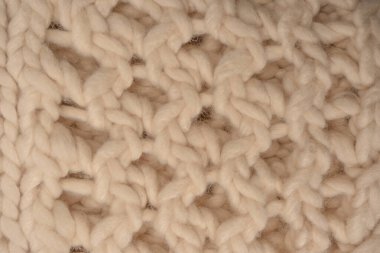 A fragment of beige knitted fabric, knitted from white sheep wool. Knitted background. 