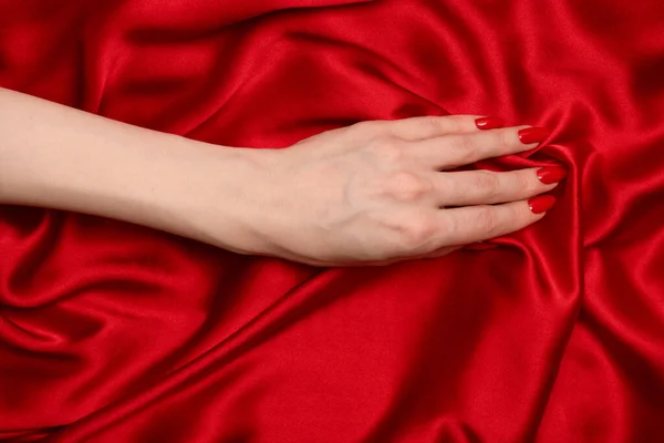 stock image Beautiful red manicure on woman hands on a luxury red silk backround. 