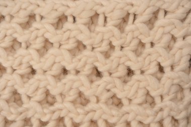 A fragment of beige knitted fabric, knitted from white sheep wool. Knitted background. 