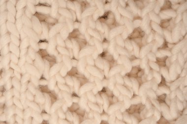 A fragment of beige knitted fabric, knitted from white sheep wool. Knitted background. 