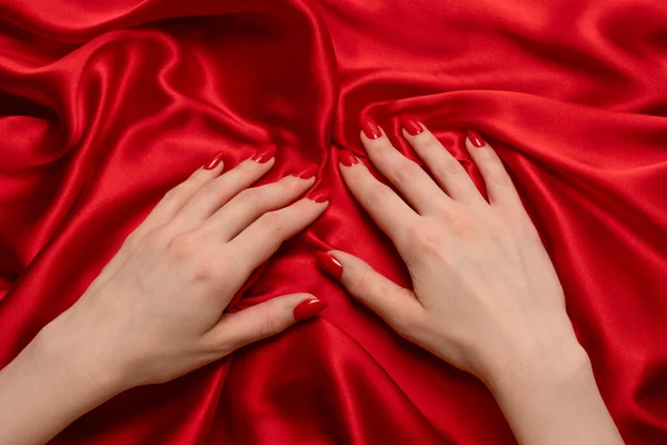 A woman's hand with red nails is trying to rip off  red silk fabric.