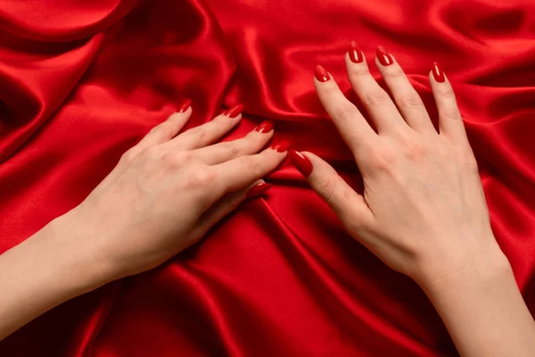 stock image Beautiful red manicure on woman hands on a luxury red silk backround. 