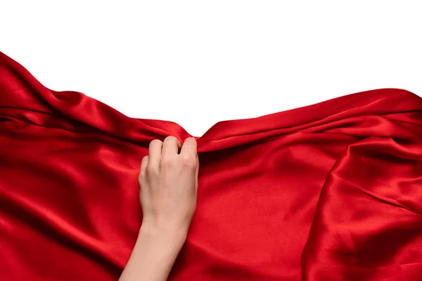 A woman\'s hand with red nails is trying to rip off  red silk fabric.