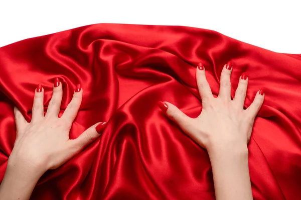 A woman\'s hand with red nails is trying to rip off  red silk fabric.