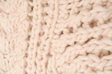 A fragment of beige knitted fabric, knitted from white sheep wool. Knitted background. 