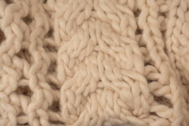 A fragment of beige knitted fabric, knitted from white sheep wool. Knitted background. 