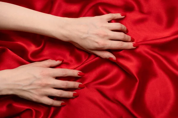 赤い爪を持つ女性の手は赤い絹の生地を破ろうとしている — ストック写真