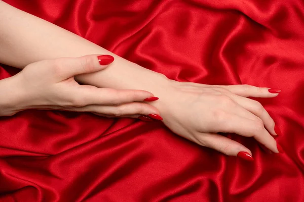 美しい赤マニキュア上の女性の手上の高級赤いシルクの背景 — ストック写真
