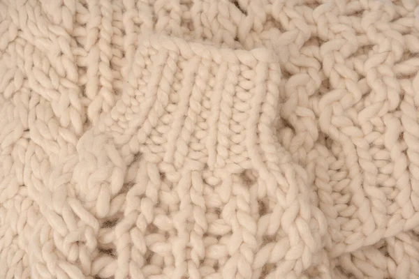 A fragment of beige knitted fabric, knitted from white sheep wool. Knitted background. 