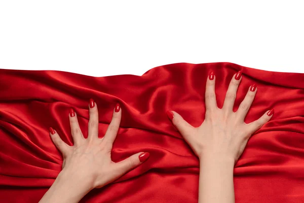 A woman's hand with red nails is trying to rip off  red silk fabric.