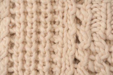 A fragment of beige knitted fabric, knitted from white sheep wool. Knitted background. 