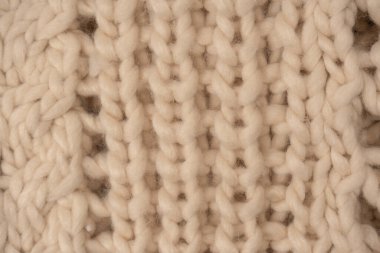A fragment of beige knitted fabric, knitted from white sheep wool. Knitted background. 