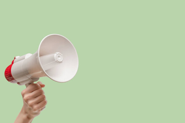 Мегафон в женских руках на зеленом фоне. Копирование пространства. 