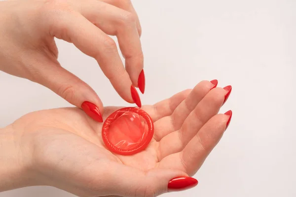 Preservativo Vermelho Uma Mão Mulher Com Unhas Vermelhas Isoladas Fundo — Fotografia de Stock