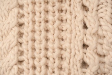 A fragment of beige knitted fabric, knitted from white sheep wool. Knitted background. 
