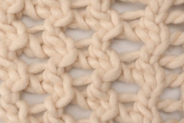 A fragment of beige knitted fabric, knitted from white sheep wool. Knitted background. 