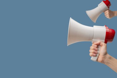 Megaphone in woman hands on a blue background.  Copy space. 