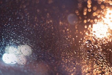 Yağmur damlaları ve ışıklarla bulanık arkaplan.