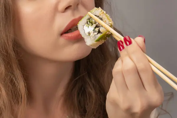 Young woman with red nails is eating sushi close up.
