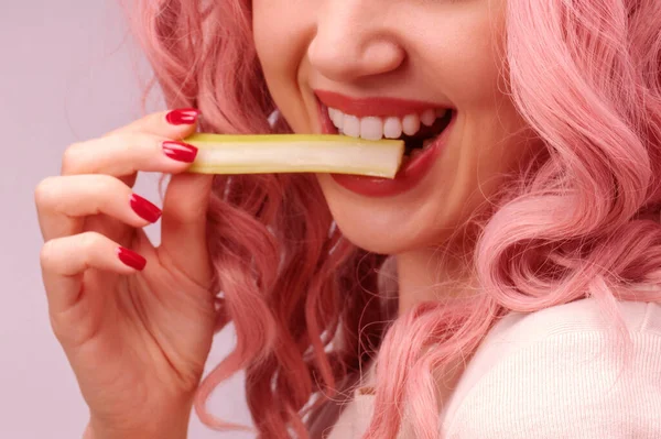 Celery sticks in a woman hand. Woman with pink curly hair is eating celery close-up.