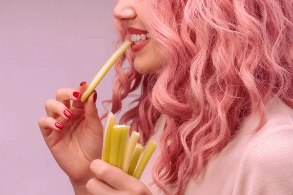 Celery sticks in a woman hand. Woman with pink curly hair is eating celery close-up.