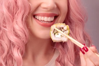 Kırmızı tırnaklı, pembe saçlı genç bir kadın suşi yiyor..