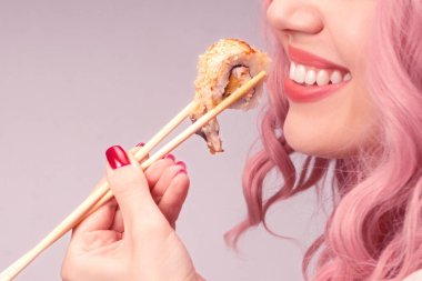 Kırmızı tırnaklı, pembe saçlı genç bir kadın suşi yiyor..