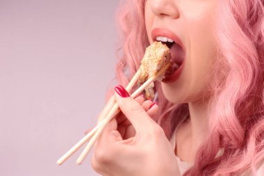 Kırmızı tırnaklı, pembe saçlı genç bir kadın suşi yiyor..