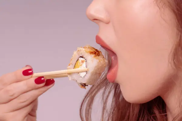 Young woman with red nails is eating sushi close up.