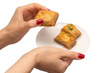 Beyaz arka planda kırmızı tırnakları olan bir kadının elindeki enfes tatlı baklava. Üst görünüm.