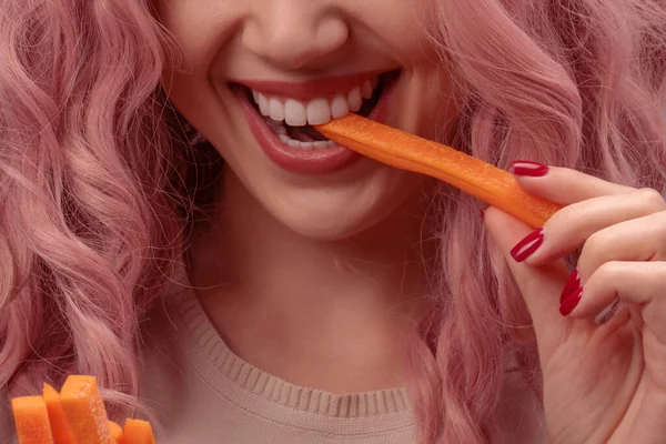 Carrots cut into strips in woman hand. Woman with pink curly hair is eating carrot close-up.