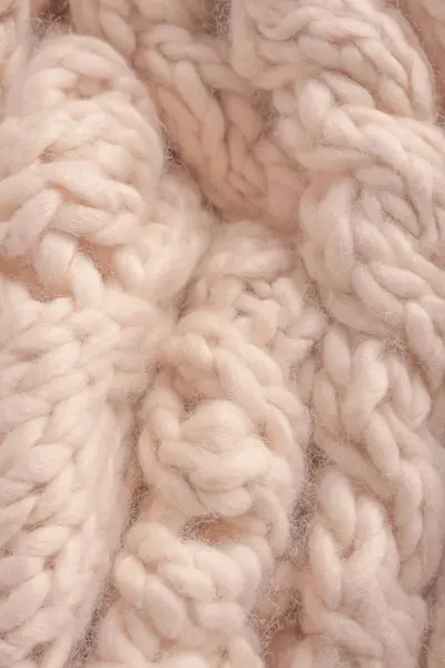 A fragment of beige knitted fabric, knitted from white sheep wool. Knitted background.