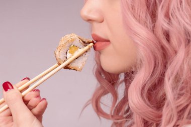 Kırmızı tırnaklı, pembe saçlı genç bir kadın suşi yiyor..