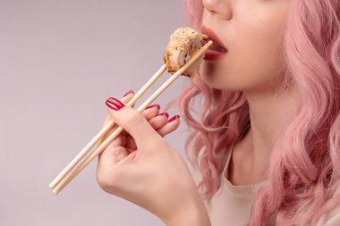 Kırmızı tırnaklı, pembe saçlı genç bir kadın suşi yiyor..