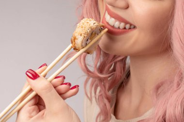 Kırmızı tırnaklı, pembe saçlı genç bir kadın suşi yiyor..