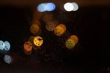 Yağmur damlaları ve ışıklarla bulanık arkaplan.