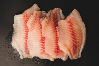 Siyah arkaplanda taze tilapia filetosu, üst görünüm. 