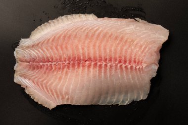 Siyah arkaplanda taze tilapia filetosu, üst görünüm. 