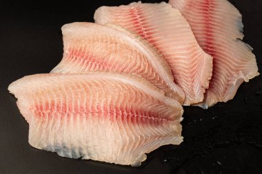 Siyah arkaplanda taze tilapia filetosu, üst görünüm. 