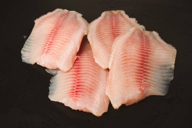 Siyah arkaplanda taze tilapia filetosu, üst görünüm. 