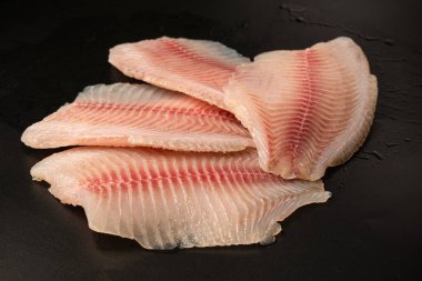 Siyah arkaplanda taze tilapia filetosu, üst görünüm. 