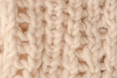 A fragment of beige knitted fabric, knitted from white sheep wool. Knitted background. 