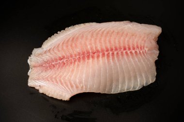 Siyah arkaplanda taze tilapia filetosu, üst görünüm. 