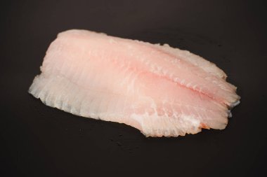 Siyah arkaplanda taze tilapia filetosu, üst görünüm. 