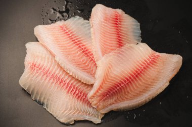 Siyah arkaplanda taze tilapia filetosu, üst görünüm. 