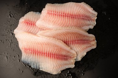 Siyah arkaplanda taze tilapia filetosu, üst görünüm. 
