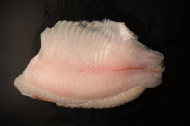 Siyah arkaplanda taze tilapia filetosu, üst görünüm. 
